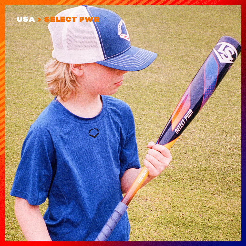 A young boy in a blue shirt and baseball cap stands on grass, looking at a colorful baseball bat labeled “SELECT PWR.” Text in the upper left reads “USA > SELECT PWR.” Red and orange border surrounds the image.