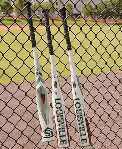 Several Louisville Slugger Atlas bats, including the 2025 Atlas (-5) 2 5/8" USSSA Baseball Bat (WBL2981010), are resting on a fence.