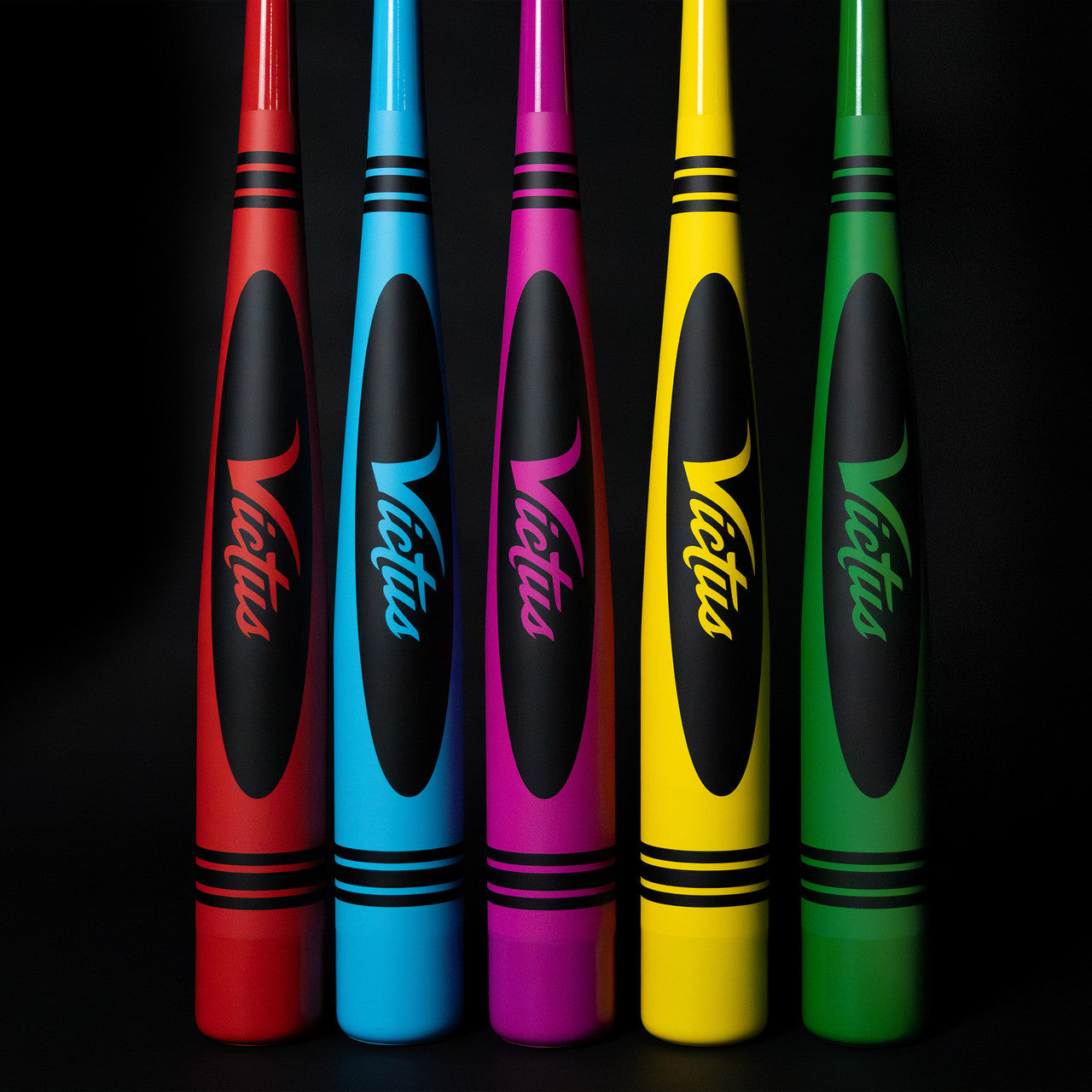 Five vibrant 2025 Victus Vibe Crayon (-10) USA Baseball Bats—red, blue, purple, yellow, and green—stand upright together. Each one-piece aluminum bat features a vibration-reducing knob and bold Victus branding.