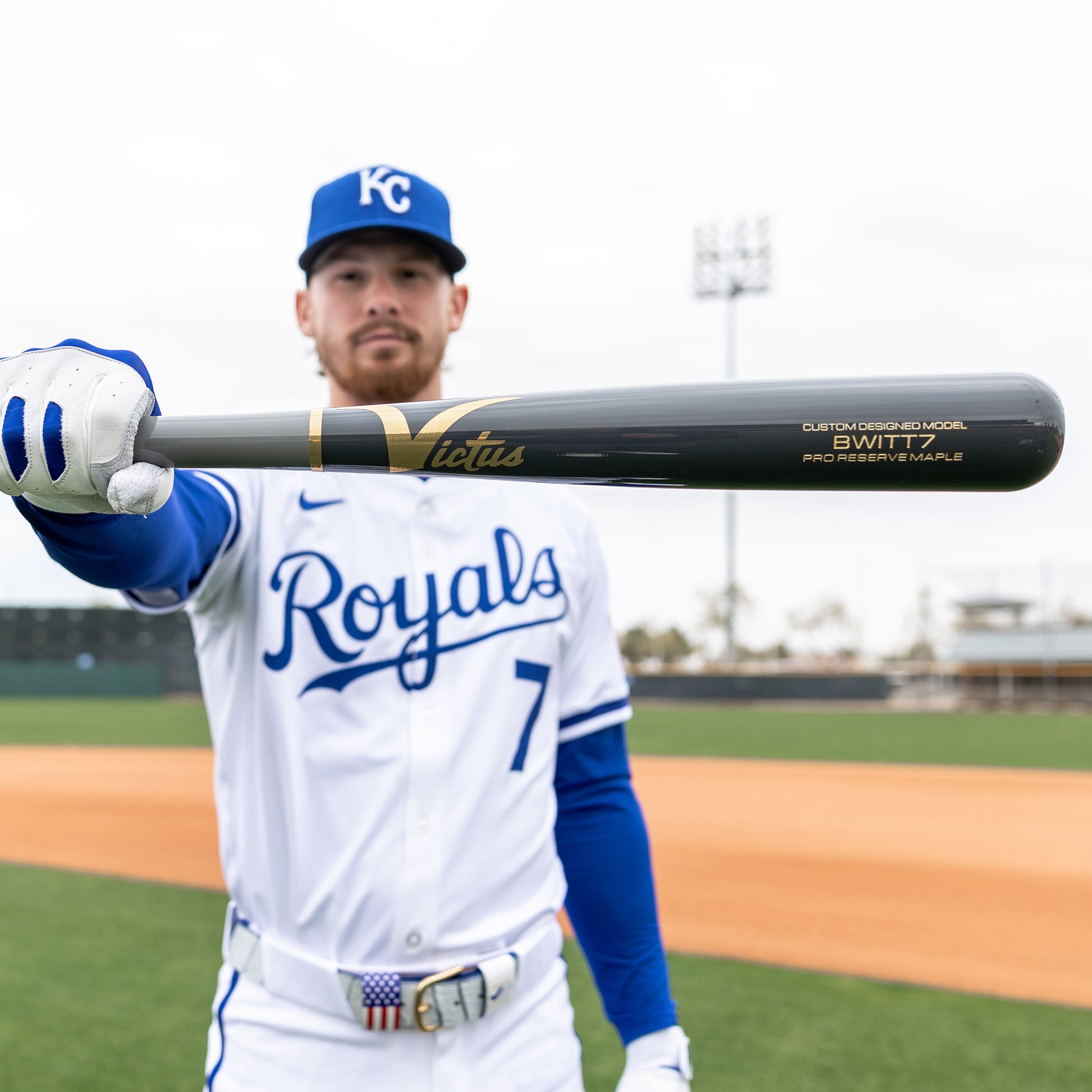 A Kansas City Royals player in uniform holds a Victus Bobby Witt Jr BWITT7 Pro Reserve Maple Wood Bat (model VRWMBWITT7) toward the camera on a baseball field, with the bat’s branding and model visible in the foreground.