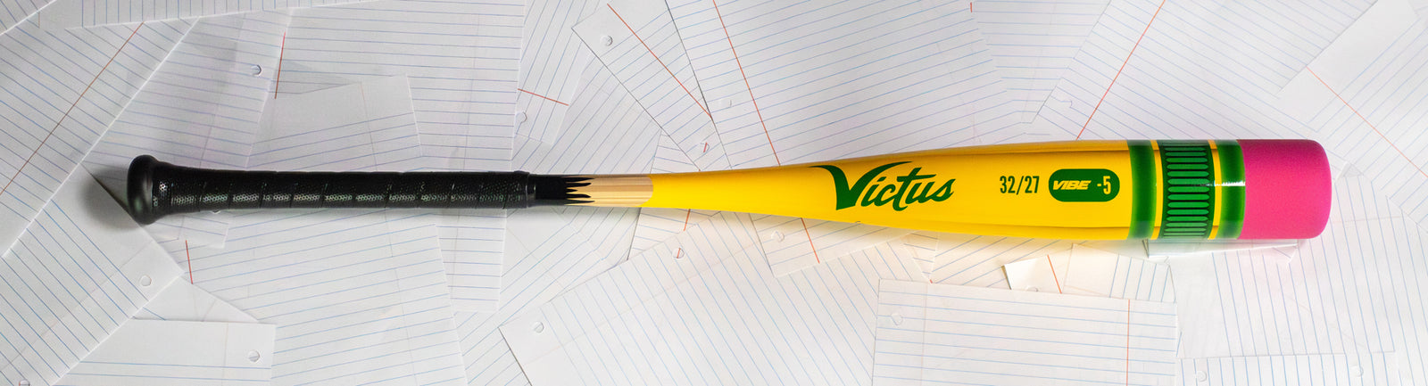 A yellow and green Victus baseball bat with a pink end cap lies diagonally on a scattered pile of lined index cards.