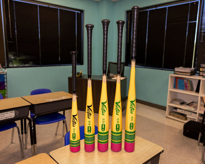 Six identical Victus Vibe Pencil (-5) USSSA baseball bats are lined up on classroom desks in a bright room—perfect for students learning the basics with this 2025 Victus VSBVIBP5 demo model before advancing to higher-level gear.