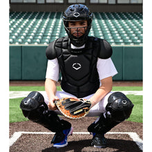 Wearing the EvoShield G2S Baseball Catcher's Gear Kit by EvoShield, a catcher crouches behind home plate with a mitt in an empty stadium.