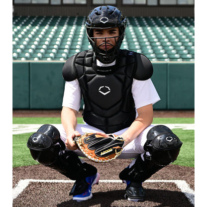 Wearing the EvoShield G2S Baseball Catcher's Gear Kit by EvoShield, a catcher crouches behind home plate with a mitt in an empty stadium.