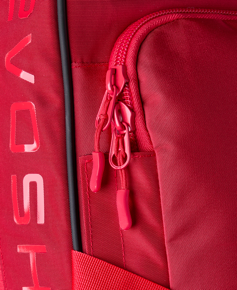 Close-up of the EvoShield Takeover Wheeled Bag (WB57572) in red, showing a zippered pocket with two red pulls, bat sleeves, and partial white EvoShield branding along the left side.