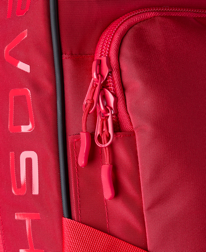 Close-up of the EvoShield Takeover Wheeled Bag (WB57572) in red, showing a zippered pocket with two red pulls, bat sleeves, and partial white EvoShield branding along the left side.