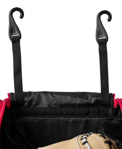 A close-up of the EvoShield Takeover Wheeled Bag (WB57572) in black and red, featuring two black straps with plastic hooks and part of a tan baseball glove visible inside the open bag.