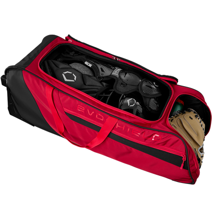 The EvoShield Takeover Wheeled Bag (WB57572) by EvoShield is unzipped, showing spacious bat sleeves and baseball equipment inside, including a helmet, catcher’s gear, and a tan glove.