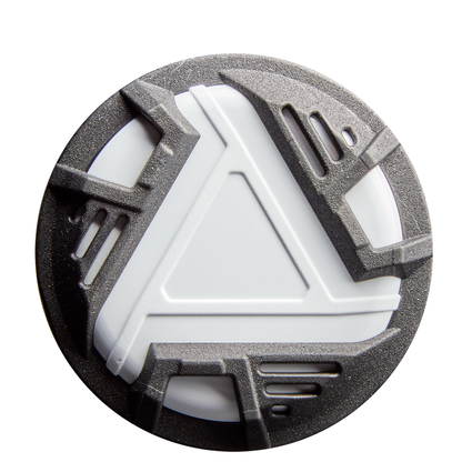 A round object with a white center and raised gray geometric patterns, featuring triangle designs and vent-like slots, reminiscent of the composite barrel on the 2026 DeMarini Lotus (-10) Fastpitch Softball Bat: WBD2606010 (DEMO), set against a white background.