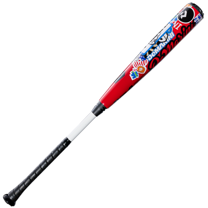 The 2026 DeMarini The Goods Sticker Bomb (-3) BBCOR Baseball Bat (WBD2653010) features a black grip, white handle, and red barrel with vibrant blue, white, and red graphics and text.