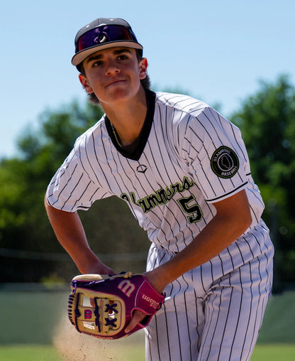 A baseball player in a white pinstripe uniform and cap gets ready to pitch, wearing a Wilson A2000 1720SS 11.5″ Baseball Glove (WBG0009401RT115) on a sunny outdoor field.