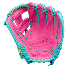 A Wilson A2000 1727SS 11.5″ Baseball Glove (model WBG0009501RT1175) by Wilson is displayed open with the palm side visible, showcasing its pink color with teal lacing and accents and SuperSnakeSkin construction against a white background.