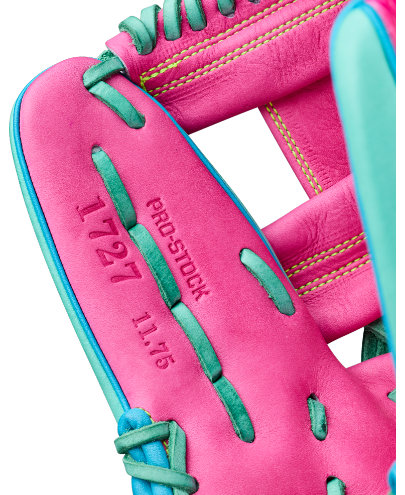 Close-up of a pink Wilson A2000 1727SS 11.5″ Baseball Glove (WBG0009501RT1175) with teal laces. The glove is crafted with SuperSnakeSkin for added durability and has “PRO-STOCK”, “1727”, and “11.75” stamped in red text on the inner palm. Yellow stitching is visible on the wrist area.