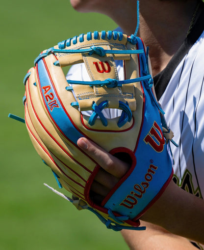 A close-up of a person wearing the Wilson A2K 1786 11.5″ Baseball Glove: WBG0010101RT115, featuring blue laces and the Wilson logo, holding it near their face. Crafted from Pro Stock Select leather, this infield glove stands out against the green grass background.
