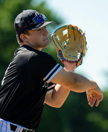 On a sunny day, a baseball player wearing a black uniform and cap throws a ball with the Wilson A2K 1786 11.5″ Baseball Glove: WBG0010101RT115, expertly crafted by Wilson from Pro Stock Select leather; sunglasses rest atop his cap.