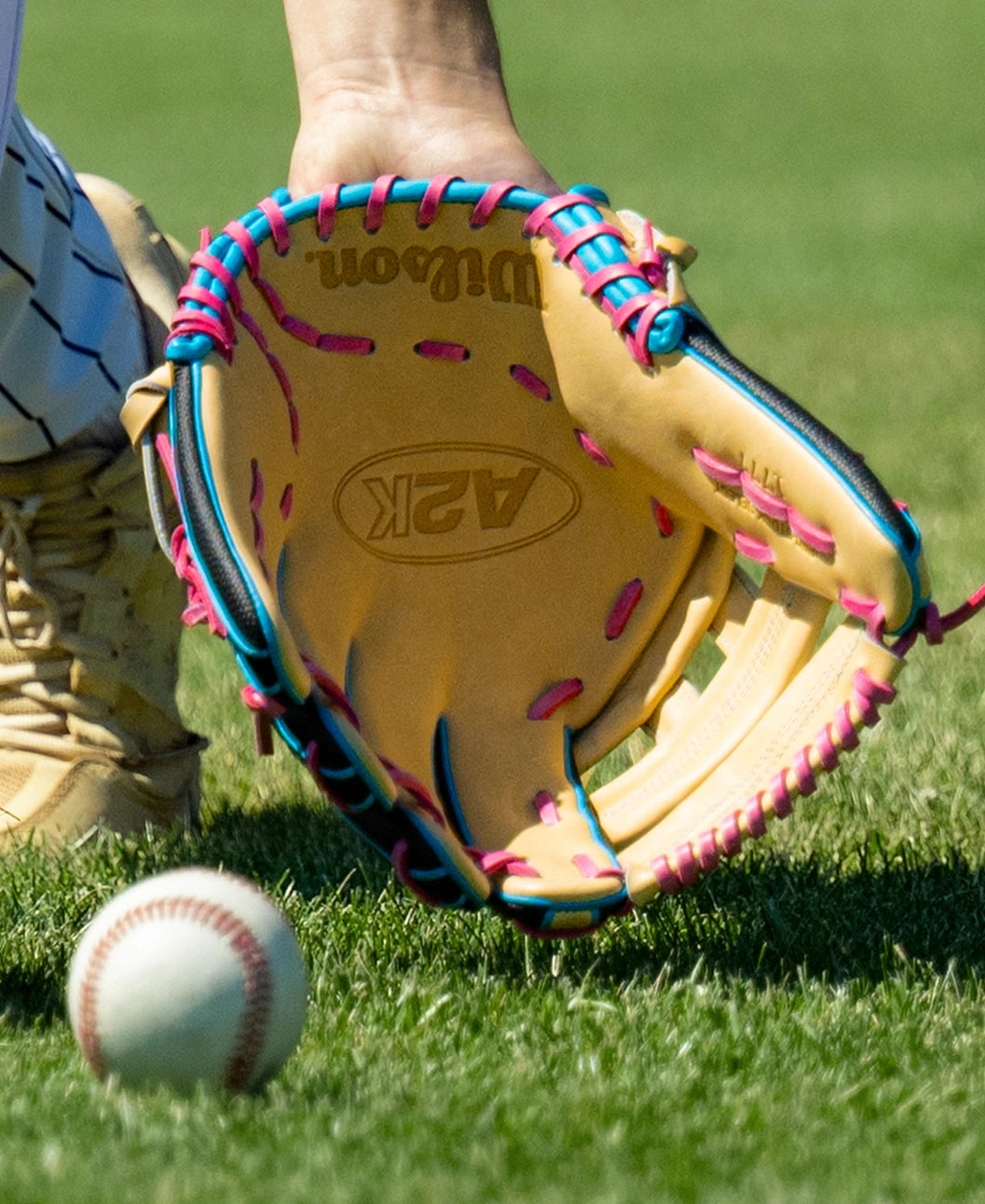 A close-up of a colorful outfield glove catching a ball on grass, with a player’s hand and part of their uniform visible. The Wilson A2K 1777 12.75″ Baseball Glove: WBG0010301 features Double Palm Construction, offering extra stability and comfort for seamless catches.