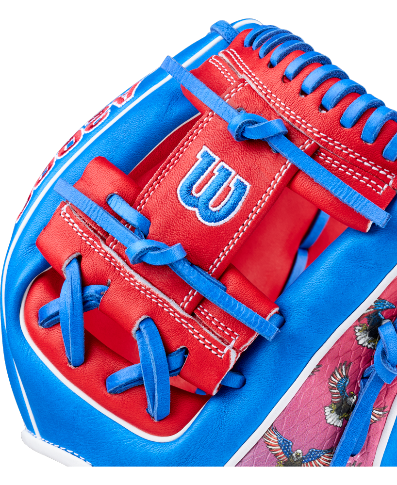 Close-up of a Wilson A2000 1786SS 11.5" Glove (GOTM July 2026) featuring red, blue, and white Pro Stock leather, blue laces, white stitching, a white W logo, and bird images on the patterned area.