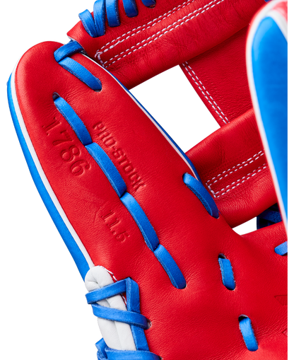 Close-up of the Wilson A2000 1786SS 11.5" Baseball Glove (GOTM July 2026) showing red Pro Stock leather with blue and white laces, embossed text, and detailed stitching—model WBG0018202RT1786.