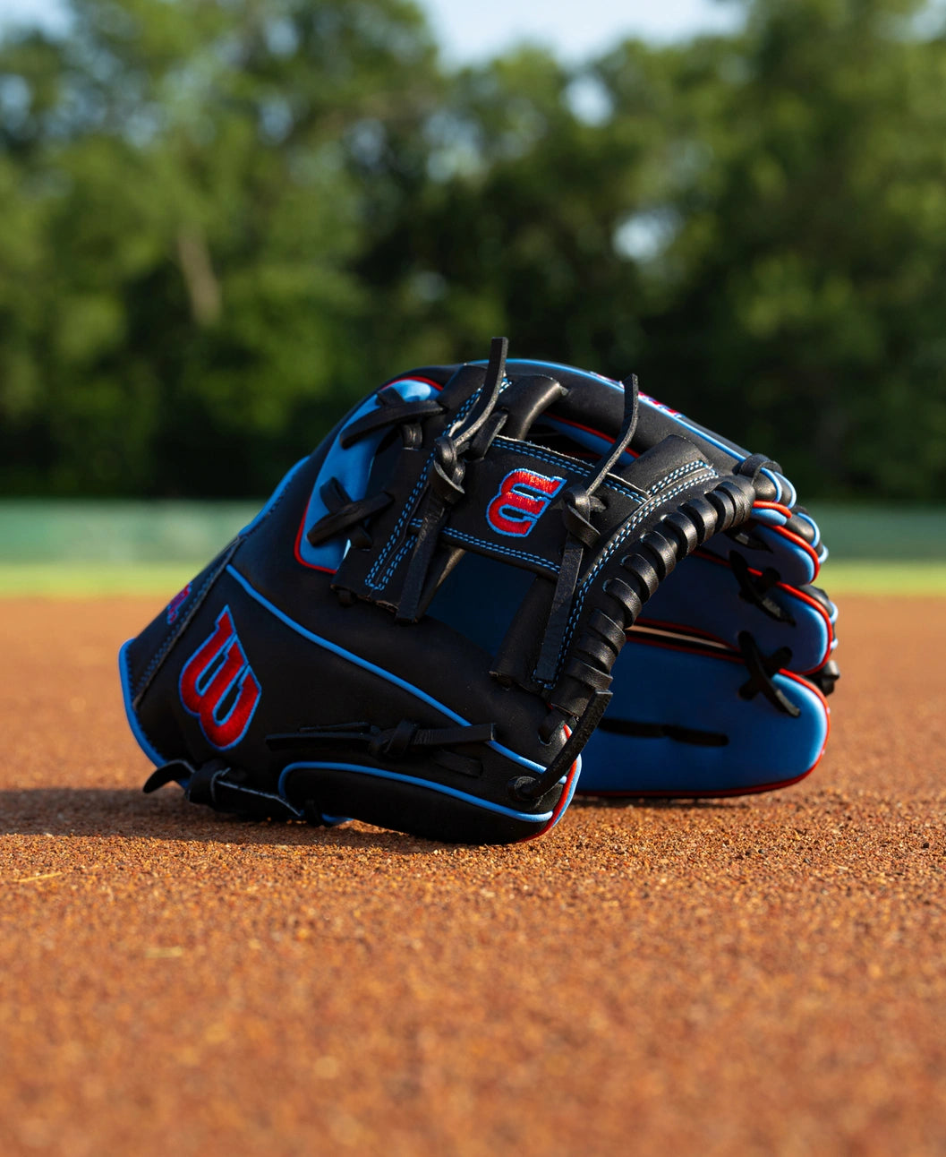 Black and blue Wilson A1000 DP15 11.5″ Baseball Glove: WBG02402RTDP15 with red accents resting on a dirt field.