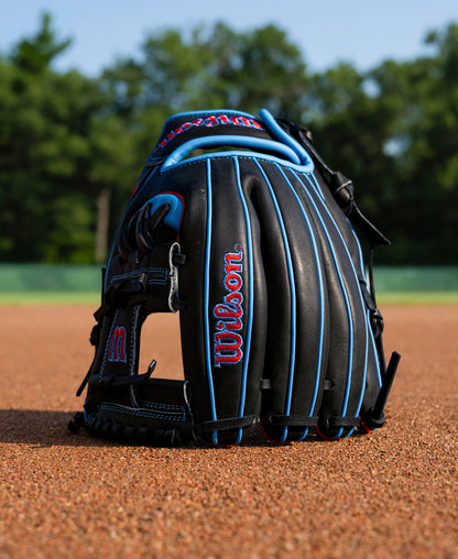 Wilson A1000 DP15 11.5″ Baseball Glove with black leather, blue piping, and red branding sitting on a dirt infield.