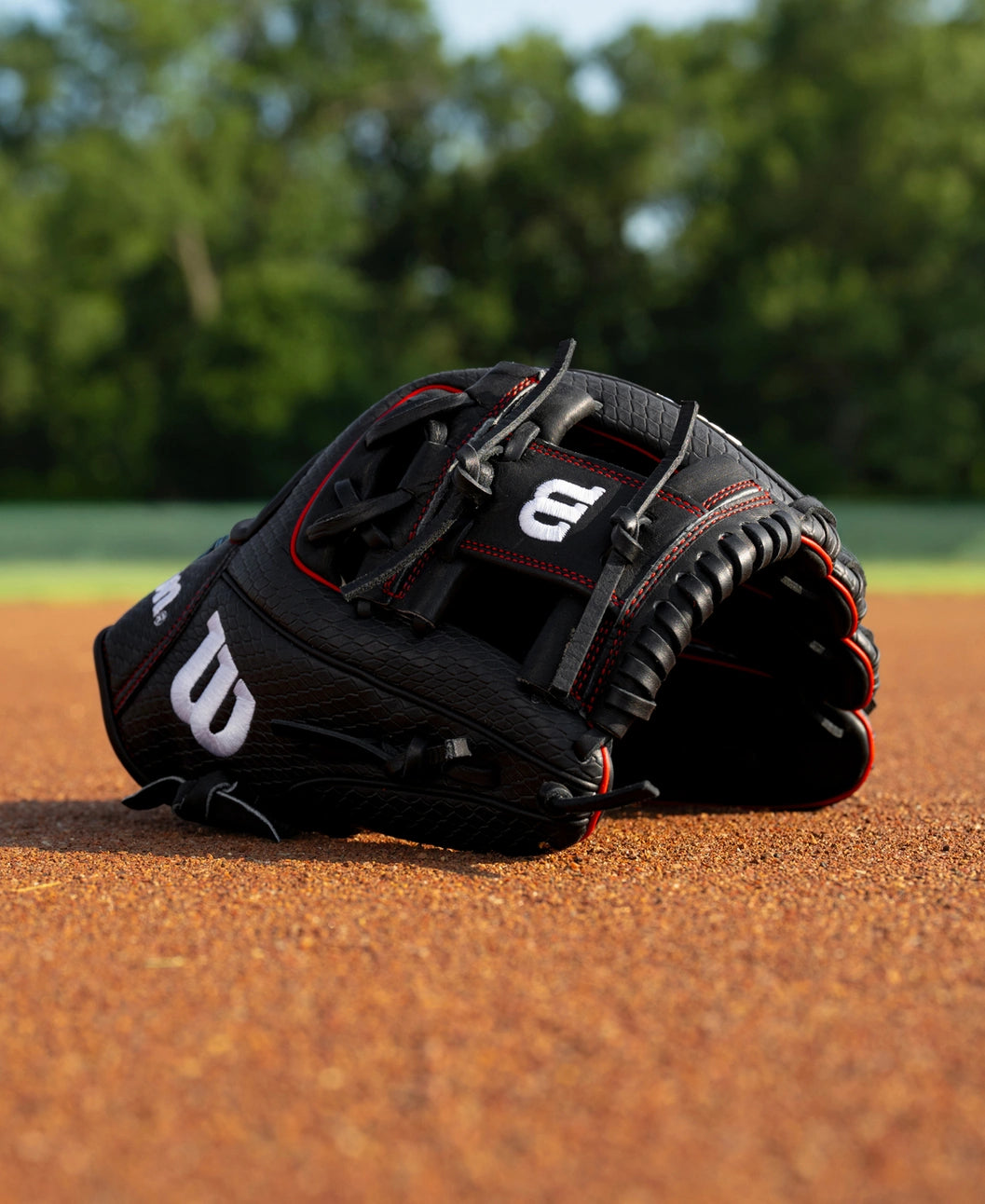 A black Wilson A1000 1975SS 11.75″ Baseball Glove: WBG02601RT1975 with red stitching resting on a dirt infield.
