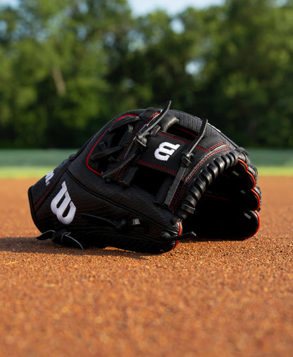 A black Wilson A1000 1975SS 11.75″ Baseball Glove: WBG02601RT1975 with red stitching resting on a dirt infield.