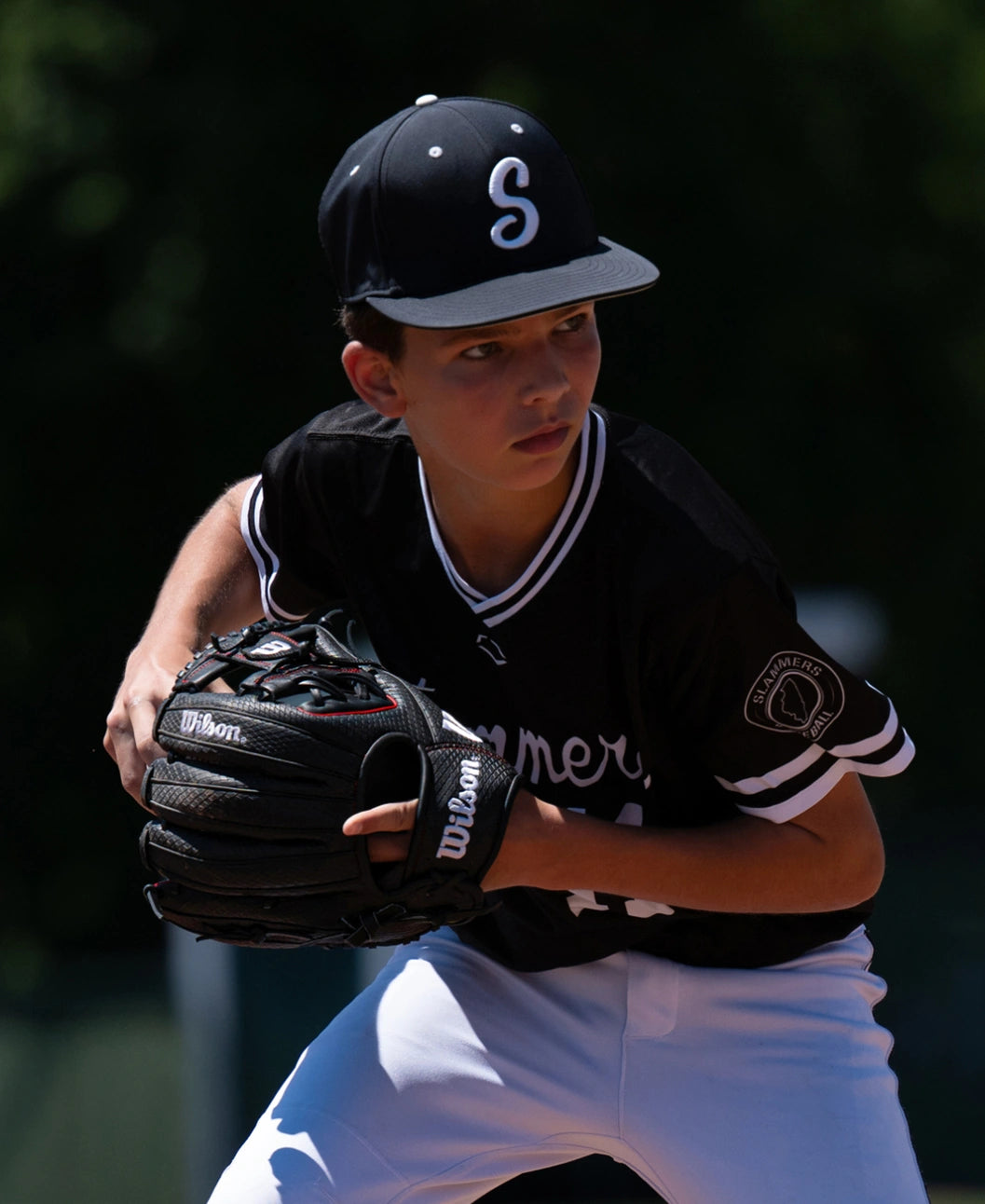 A baseball player in a black uniform and cap holds a Wilson A1000 1975SS 11.75″ Baseball Glove: WBG02601RT1975 in a ready position.