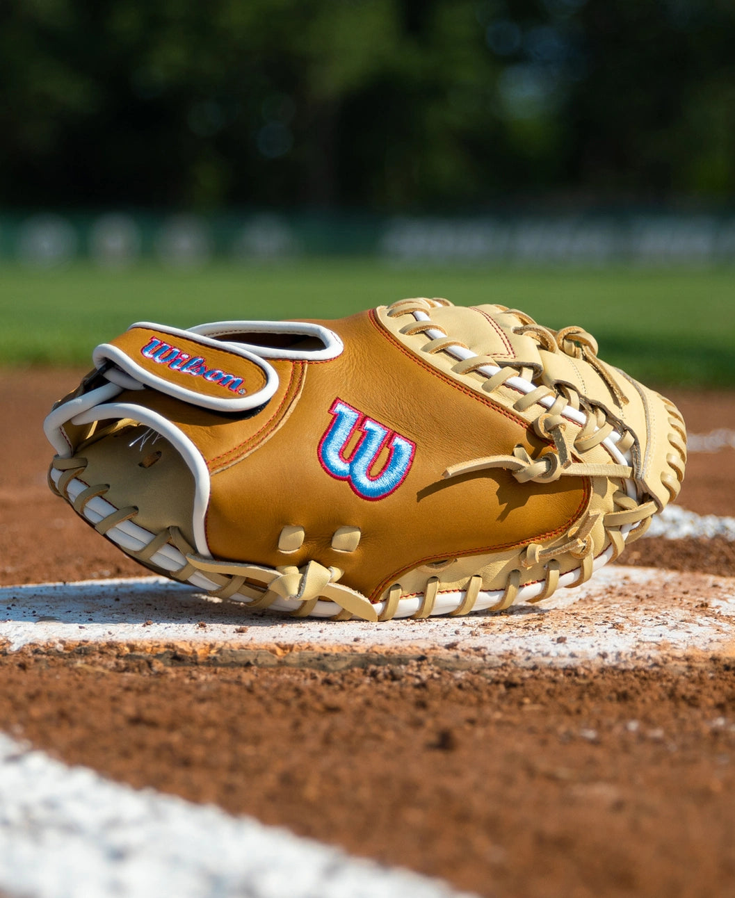 A tan and white Wilson A1000 PF33 33″ Baseball Catcher’s Mitt: WBG03001RTPF33 rests on a baseball diamond.