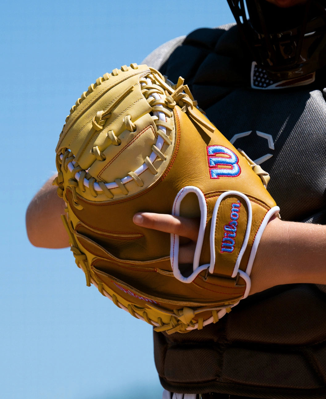 A tan Wilson A1000 PF33 33″ Baseball Catcher’s Mitt: WBG03001RTPF33 with white lacing, held by a player in chest protection.