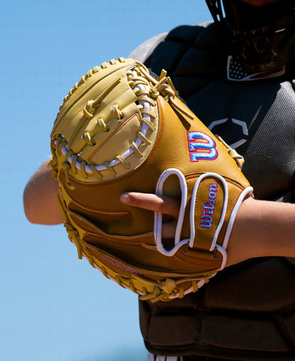 A tan Wilson A1000 PF33 33″ Baseball Catcher’s Mitt: WBG03001RTPF33 with white lacing, held by a player in chest protection.