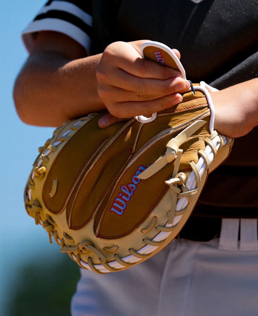 A close-up of a person wearing a tan Wilson A1000 PF33 33″ Baseball Catcher’s Mitt: WBG03001RTPF33 with white lacing.
