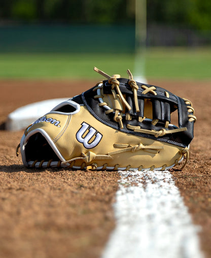 Wilson A1000 PF1612 12″ Baseball First Base Mitt in tan and black resting on a dirt baseball field.
