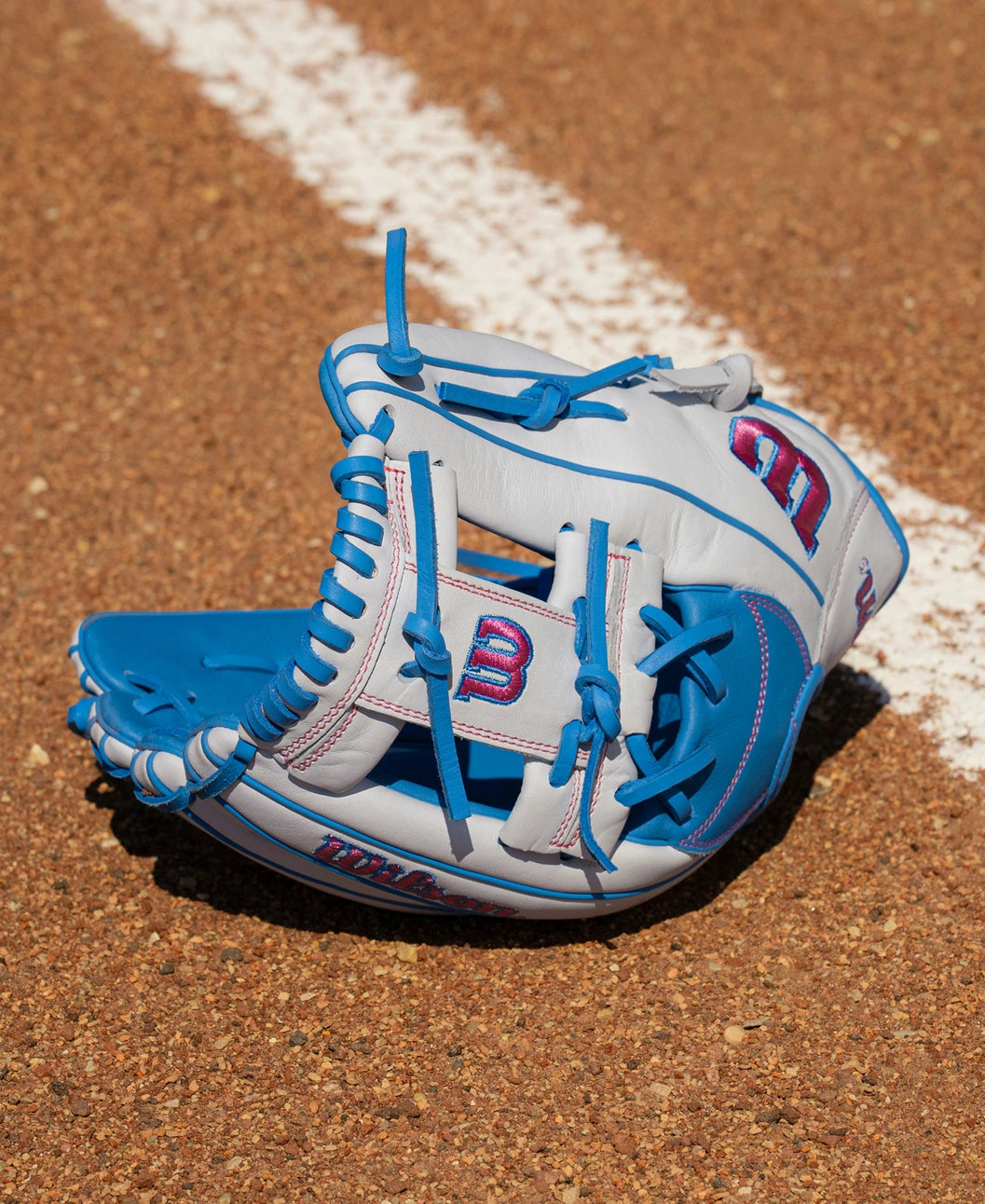 Gray and blue Wilson A1000 H12 12″ Fastpitch Glove: WBG03201RTH12 with pink accents resting on a dirt field.