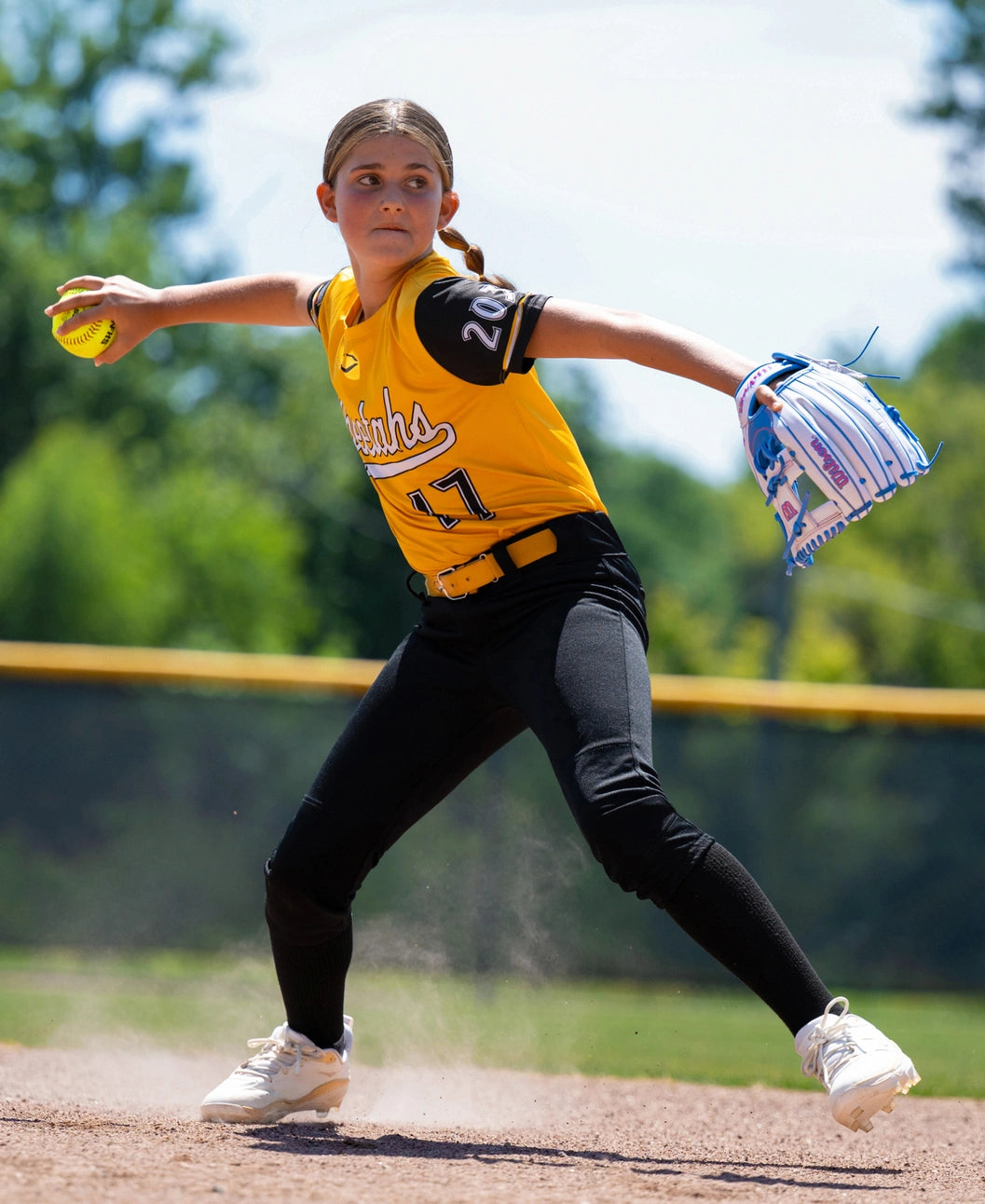 A young softball player in a yellow and black uniform throws a yellow ball while wearing a white and blue Wilson A1000 H12 12″ Fastpitch Glove: WBG03201RTH12.