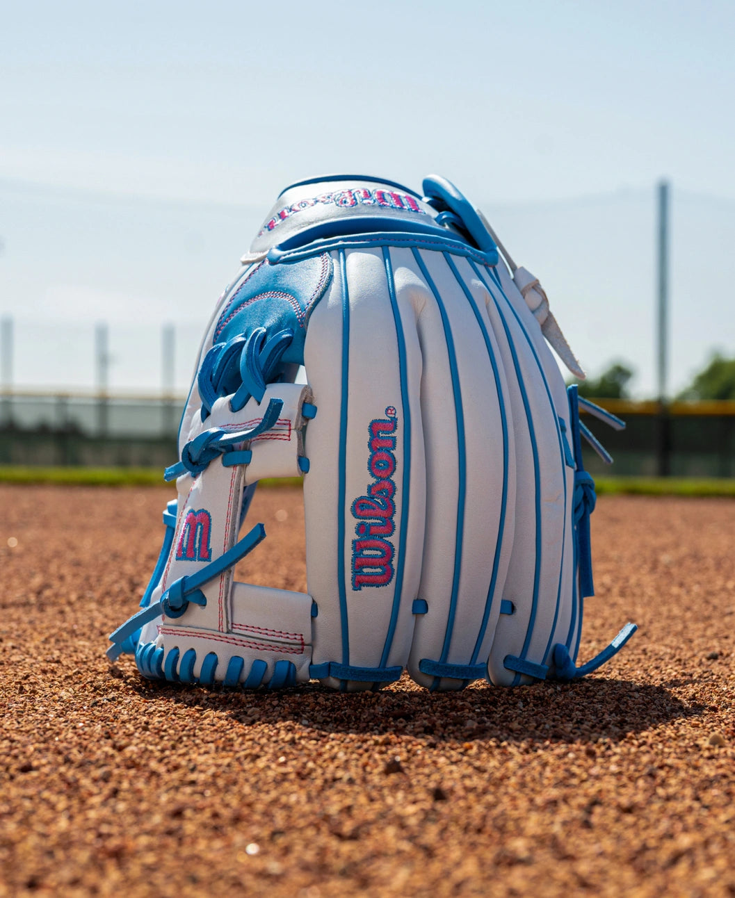 White and blue Wilson A1000 H12 12″ Fastpitch Glove: WBG03201RTH12 sitting on a dirt infield.