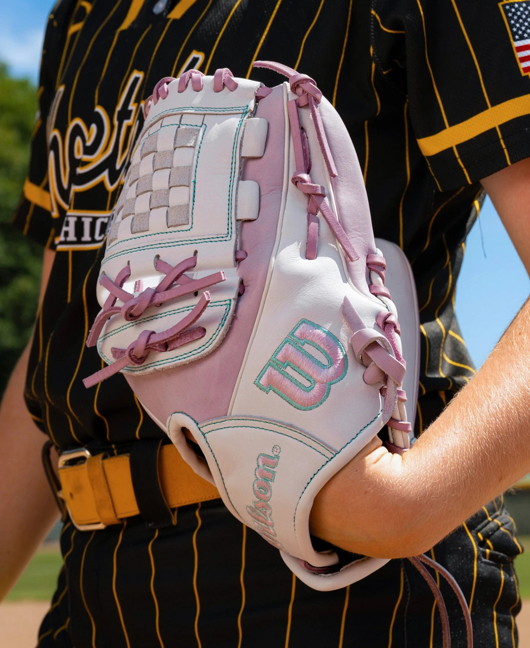 A player wearing a white and light purple Wilson A1000 P12 12″ Fastpitch Glove: WBG03401RTP12 with a checkered web.