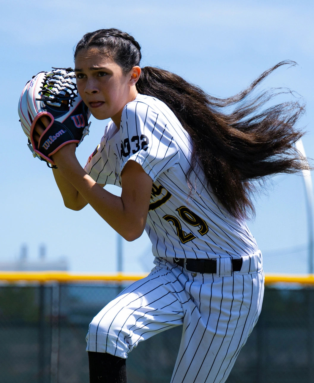 A softball player in a pinstriped uniform prepares to catch a ball with her Wilson A1000 T125 12.5″ Fastpitch Glove.