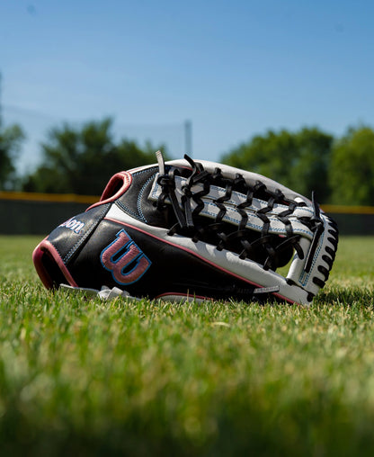 A black and white Wilson A1000 T125 12.5″ Fastpitch Glove: WBG03501RTT125 with pink accents resting on a grass field.