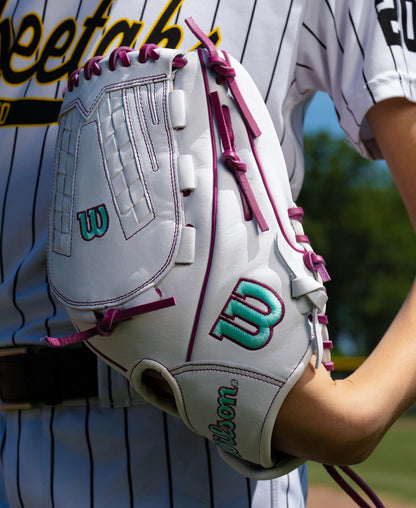 Wilson A1000 V125 12.5″ Fastpitch Glove in white with purple lacing and teal accents worn on a player’s hand.