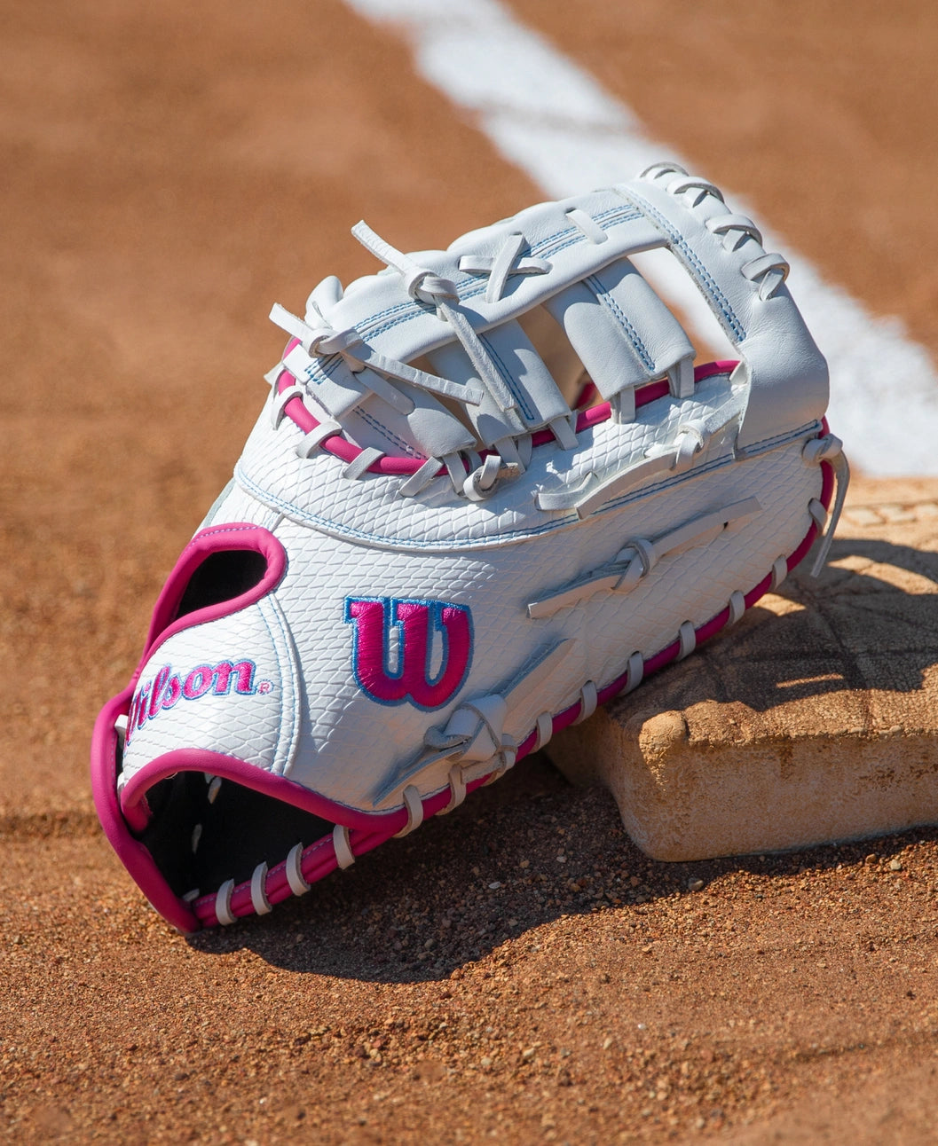 Wilson A1000 FP1620SS 12.5″ Fastpitch First Base Mitt with pink accents resting on a base on a dirt infield.