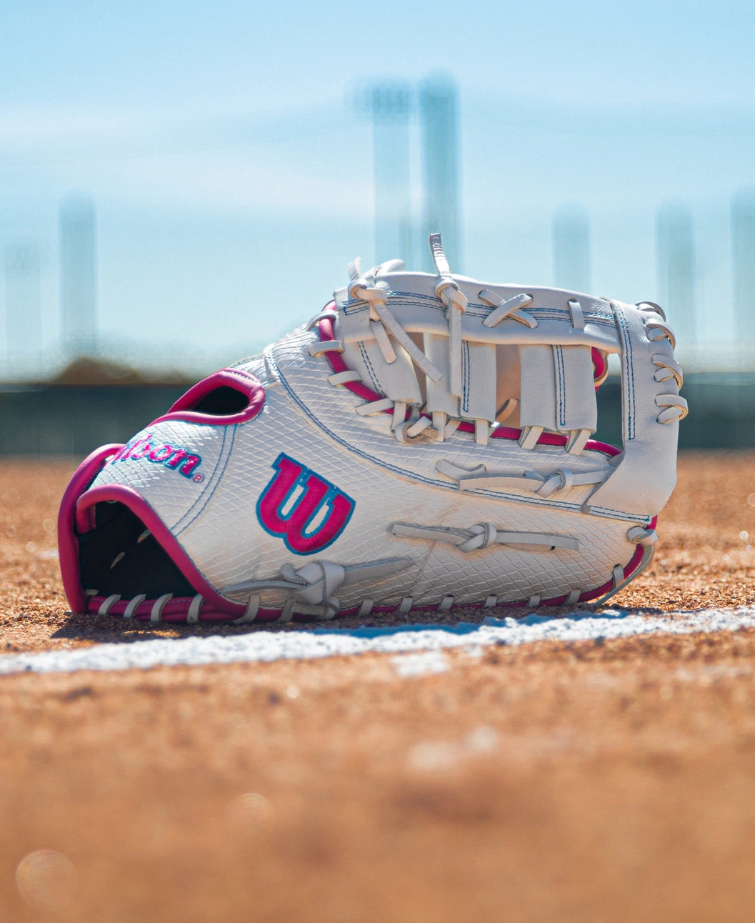 White and pink Wilson A1000 FP1620SS 12.5″ Fastpitch First Base Mitt sitting on a dirt field.