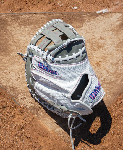 White and grey Wilson A1000 FPCM33 33″ Fastpitch Catcher’s Mitt: WBG03801RTFC33 with pink stitched accents on a dirt surface.