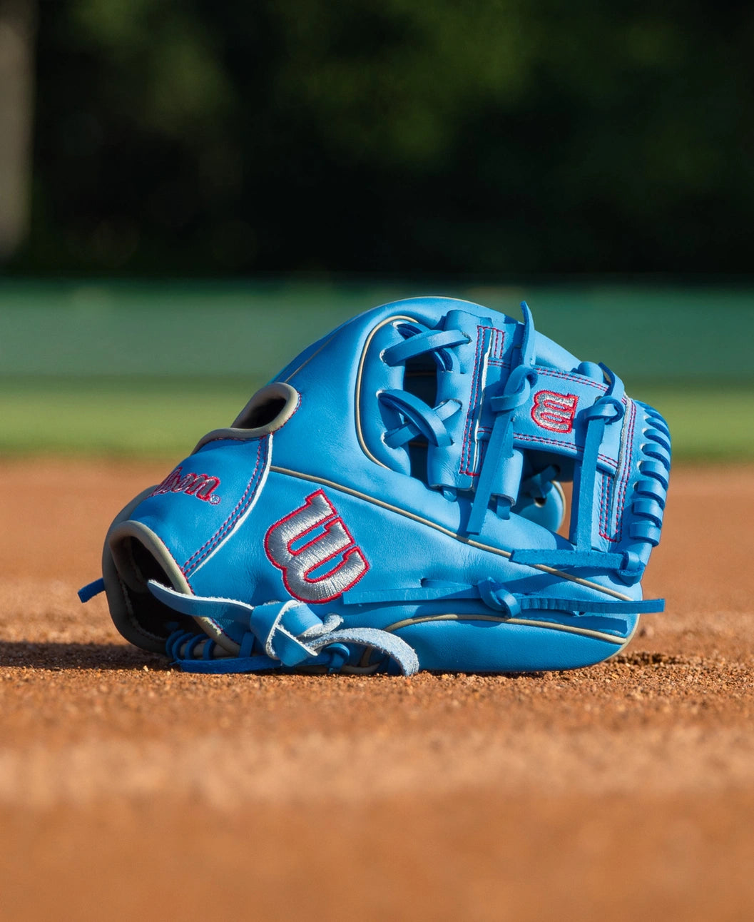 Light blue Wilson A900 11.25″ Baseball Glove: WBG03901RT1125 with red stitching and red logos resting on a dirt infield.