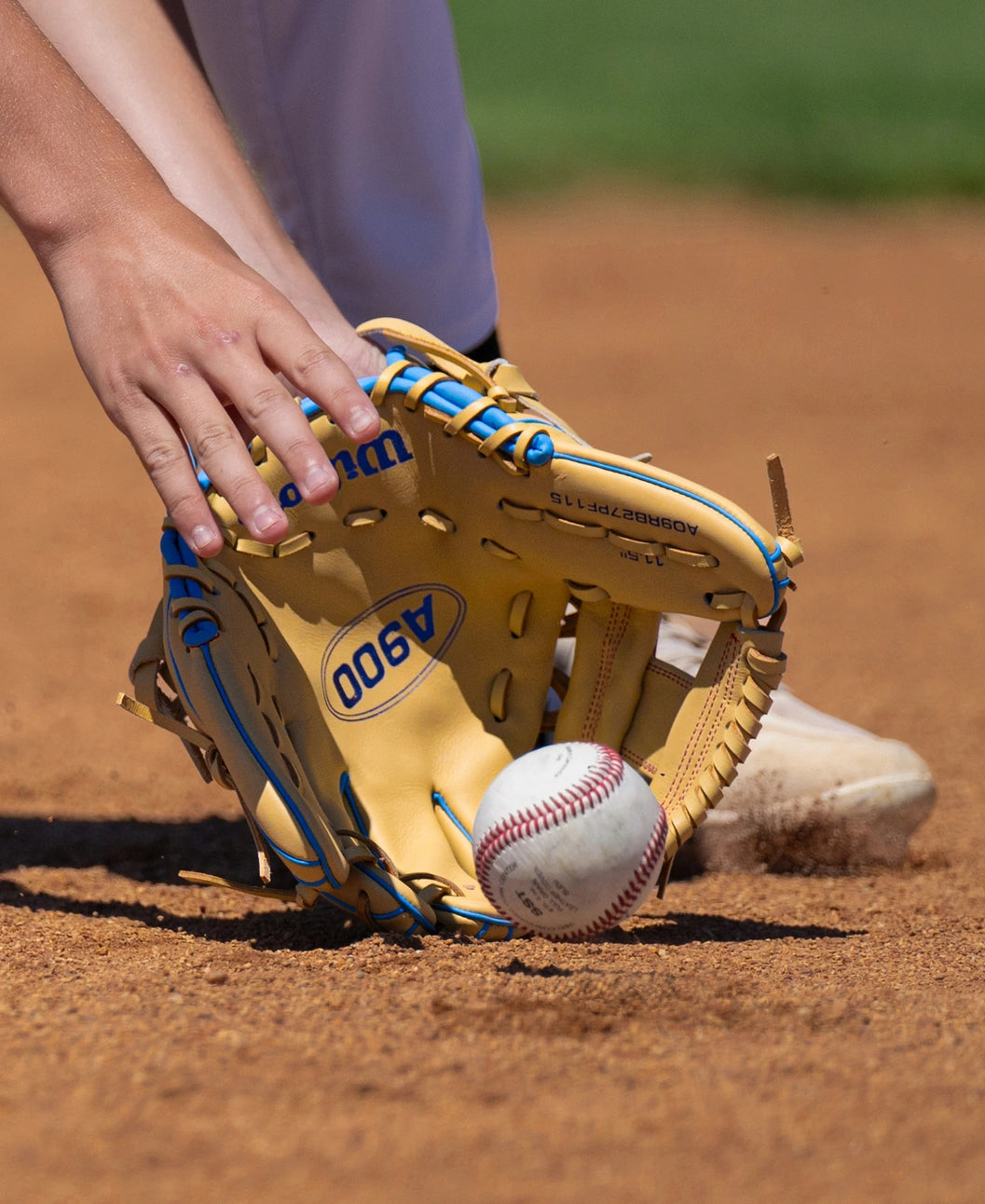 A tan Wilson A900 11.5″ Baseball Glove: WBG04002RT115 scooping a baseball off a dirt field.
