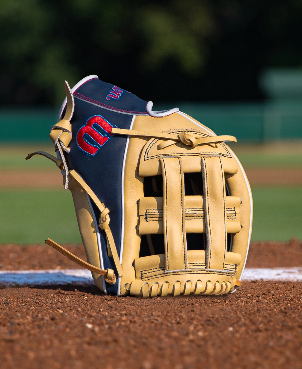 Wilson A900 12″ Baseball Glove: WBG04101RT12 in tan and navy blue full grain leather with an H-web design, resting on a dirt pitcher’s mound.