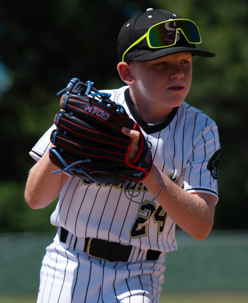 A young baseball player wearing a pinstripe uniform and yellow-rimmed sunglasses holds a full-grain leather Wilson A700 11.5″ Baseball Glove: WBG04401RT115.