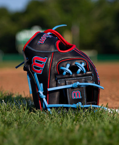 Wilson A700 11.5″ Baseball Glove: WBG04401RT115 made of black full grain leather with bright red and light blue trim, sitting on the grass of a baseball field.