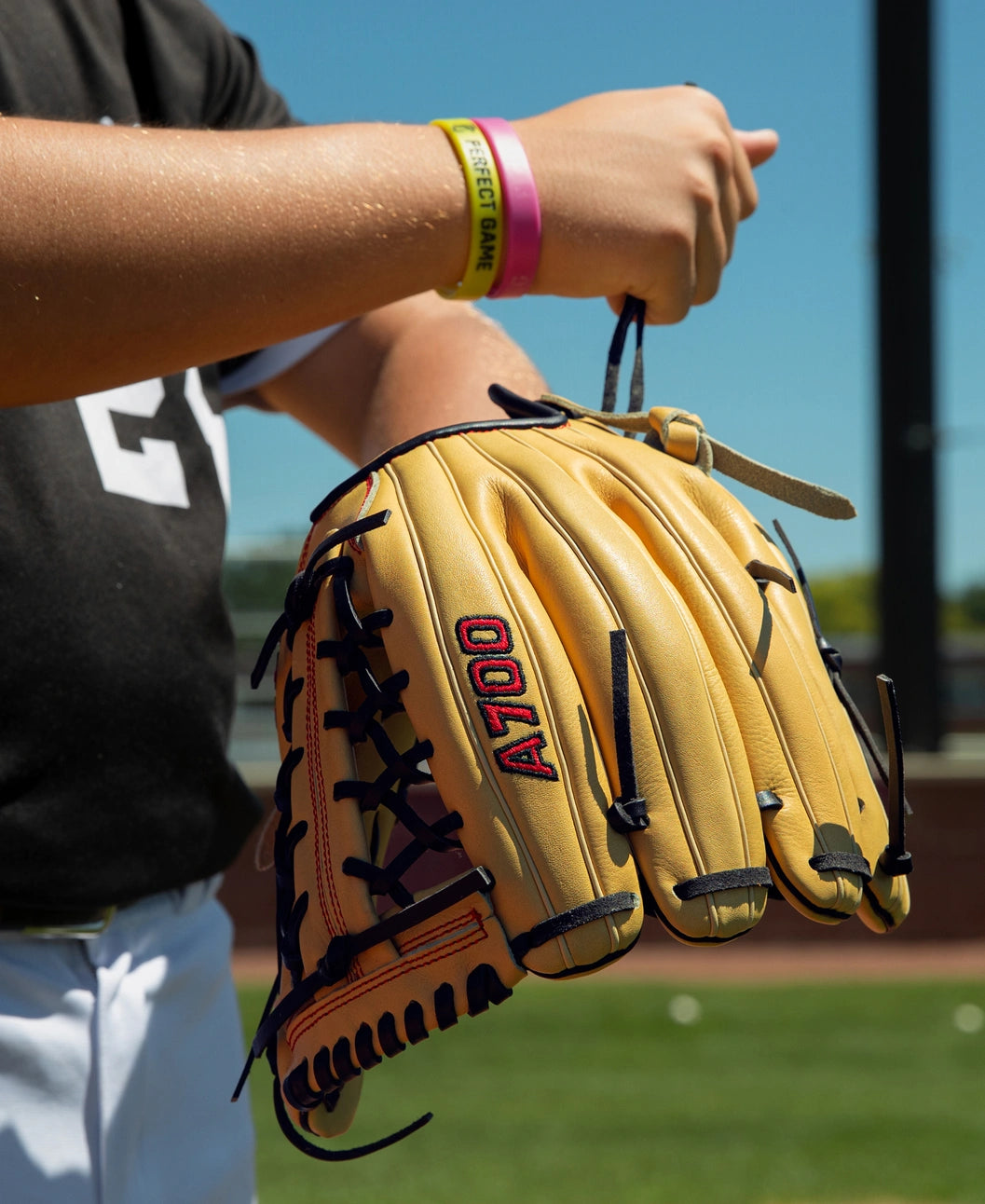A tan, full-grain leather Wilson A700 12″ Baseball Glove: WBG04501RT12 with black lacing held up by a player on a baseball field.