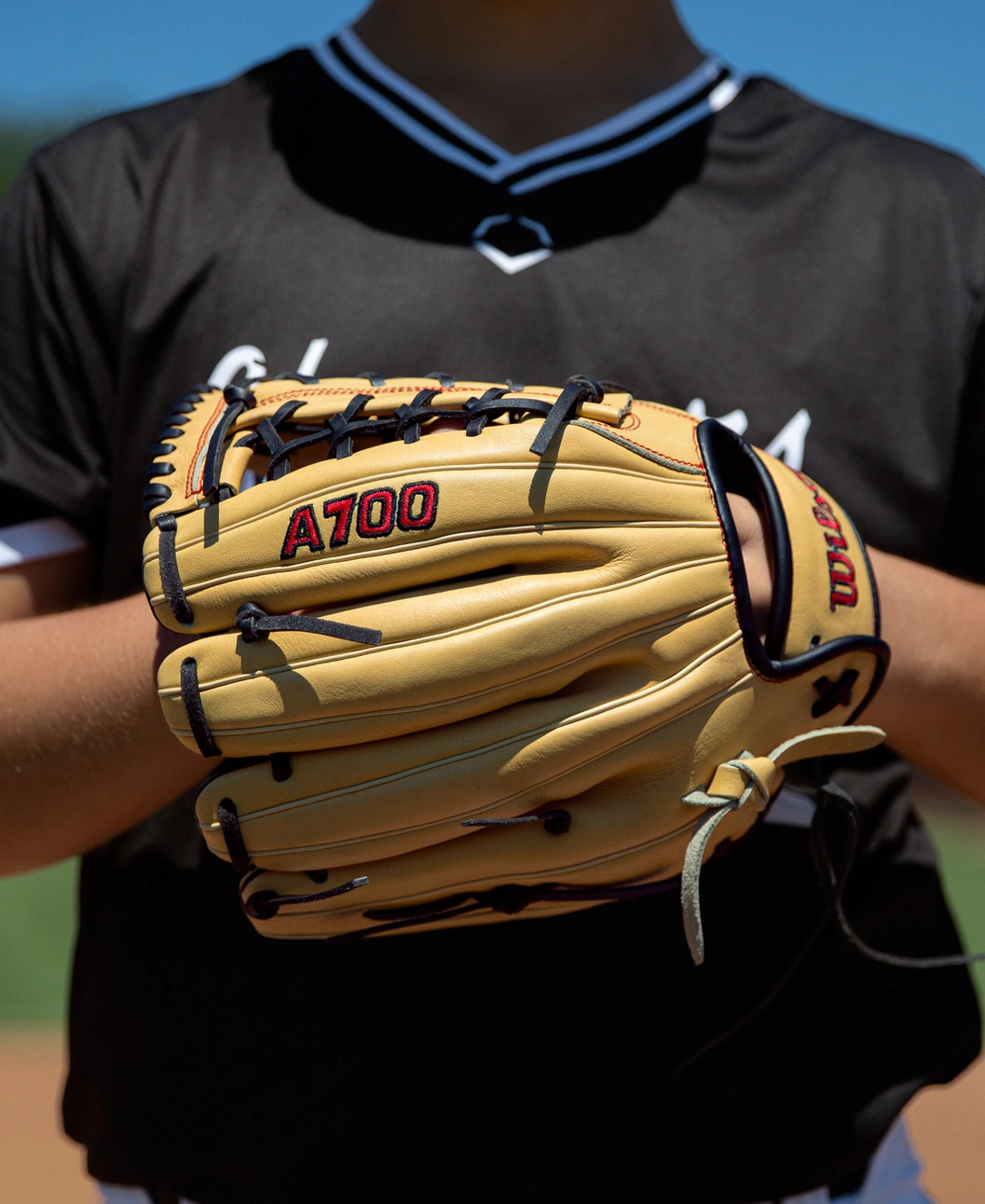 A tan Wilson A700 12″ Baseball Glove: WBG04501RT12 with black lacing held by a player in a black jersey.