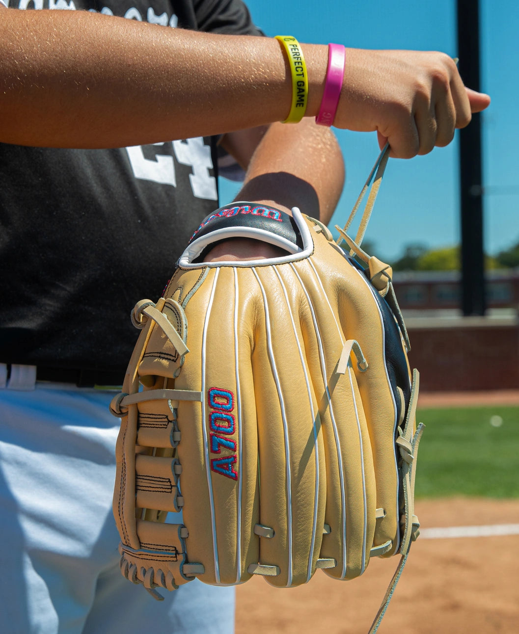 A person holding a tan Wilson A700 12.5″ Baseball Glove: WBG04601RT125 with red lettering on a baseball field.
